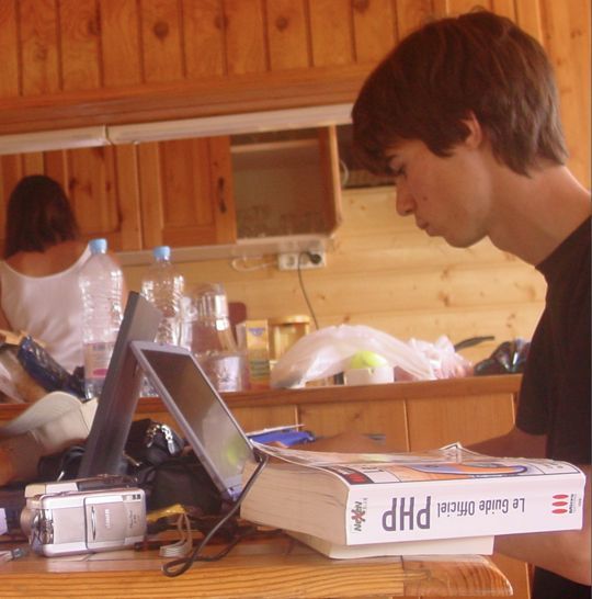 Fabien étudiant devant un ordinateur portable, le guide officiel PHP posé à côté
